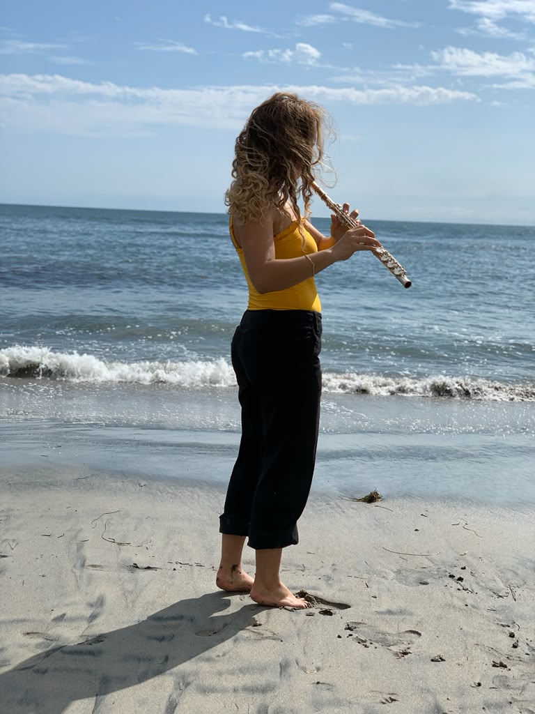 Gabriela Beltrán playing flute barefoot on the beach at the water's edge
